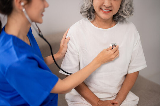Dedicated Asian nurse healthcare professional performs gentle health checkup for an adult elderly woman patient providing compassionate home care