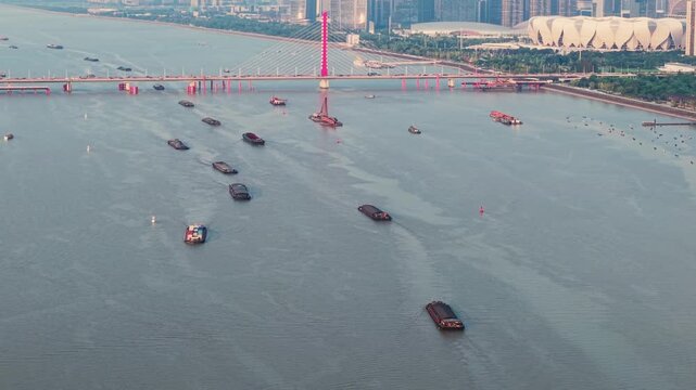 Cargo ships and boats navigate the Qiantang River in Hangzhou China. A red bridge spans the river, with the city skyline visible in the distance