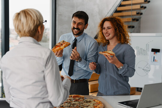 Three business people eating pizza during a lunch break in the office. Colleagues enjoying casual teamwork and relaxation time - Powered by Adobe