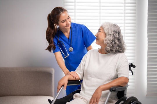 Asian adult nurse provides compassionate home care for older woman in wheelchair elderly support healthcare assistance happy patient comfort medical professional