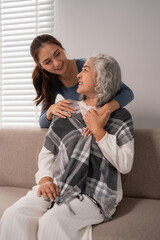 Asian young woman embraces loving elderly grandmother demonstrating gentle home care family bond support and affection