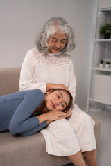 Asian women intergenerational family comfort adult daughter resting on older mother lap in home living room affectionate bond support wellbeing