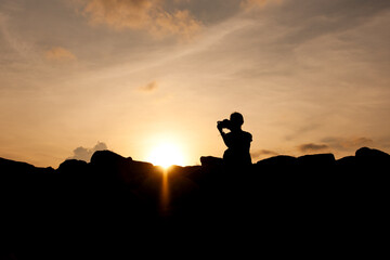 Silhouette of a Woman Photographer at Sunset on a Rocky Shore
