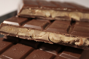 Milk chocolate bar broken to reveal creamy peanut filling inside stacked on chocolate pieces showing cross-section and texture