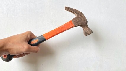 Hand holding an iron hammer with an orange and black handle in front of a plain white background. The concept of manual labor, artisan tools, and construction work with a simple and realistic feel.