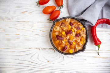 Stewed meat with vegetables and beans in a skillet on a white background in a rustic style with copy space