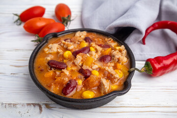 Stewed meat with vegetables and beans in a skillet on a white background in a rustic style