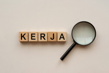 A Flat-Lay Photograph of Wooden Letter Blocks Spelling "KERJA" (Work) with a Magnifying Glass