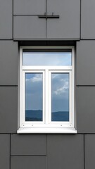 A white window reflects sky, set in a dark grey, tiled facade