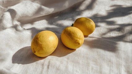 Three yellow lemons lined up on pale linen with soft shadows. Concept Lemons on Linen, Soft Shadow Lighting, Still Life Citrus, Minimalist Yellow, Textured Pale Linen