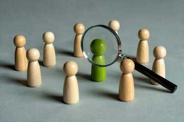 A Minimalist Business Concept Photograph Showing a Green Wooden Figure Under a Magnifying Glass for Talent Search