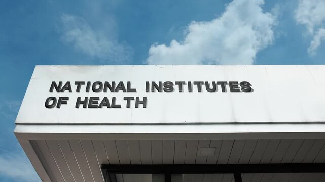 A National Institutes of Health word sign displayed on a large research facility under a clear blue sky, symbolizing medical science, public health, and biomedical research
