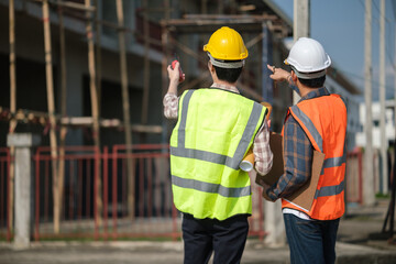 Two engineers in helmets and safety vests point at the structure during a construction site...