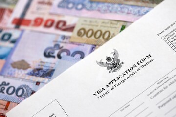 Visa application form to enter Thailand on table with thai money bills close up