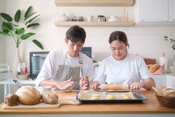 Young couple baking together at home, rolling dough and preparing cookies in a bright modern kitchen.