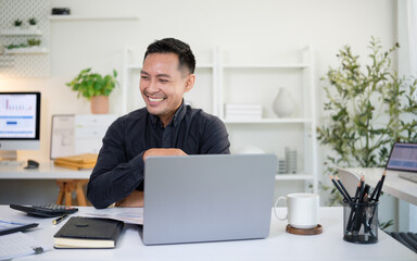 Smiling businessman sitting at desk with laptop in modern office.