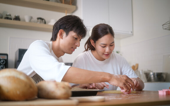 Young couple baking cookies together in a warm, minimalist kitchen, smiling and focused on shaping dough with cookie cutters. - Powered by Adobe