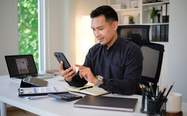 Fototapeta premium Confident businessman using smartphone at modern office desk with laptop and documents.
