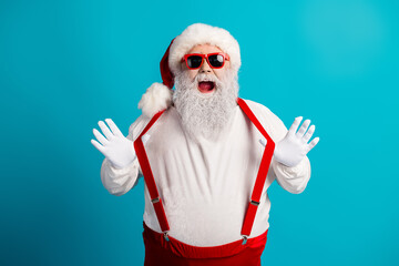 Festive Santa with red suspenders and hat posing against a blue background for Christmas themed...