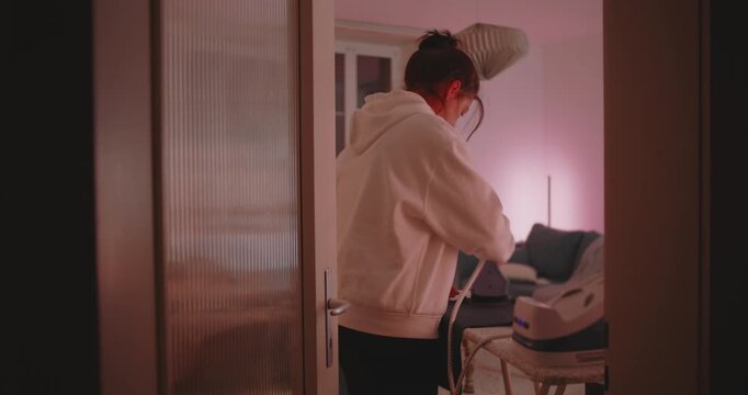 Woman ironing clothes in quiet home interior at night, showing focus and domestic responsibility in peaceful everyday moment