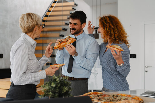Three business people eating pizza during a lunch break in the office. Colleagues enjoying casual teamwork and relaxation time