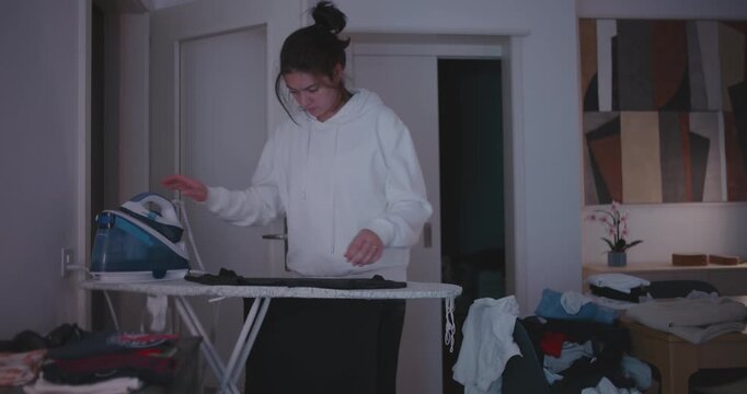 Woman ironing clothes surrounded by folded laundry, representing home organization, routine, and quiet perseverance in modern domestic life