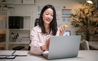 Cheerful businesswoman chatting during a remote meeting while holding a sticky note.