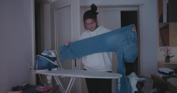 Woman pulling jeans from pile of clothes to iron, depicting everyday household routine, organization, and domestic responsibility at home