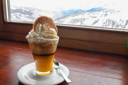 Bombardino - an Italian hot cocktail made with egg liquor (Advocaat) and brandy. Served in a glass mug with fresh whipped cream and a biscuit in an alpine bar in an Italian ski resort.