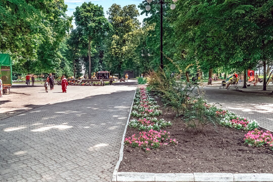 Beautiful flower beds with blooms in Shevchenko City Park in Romny. Families enjoying summer day at Ukrainian municipal park with playground and green spaces. Romny, Ukraine - June 29, 2024