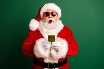 Santa Claus uses a smartphone during Christmas celebration in a green studio backdrop