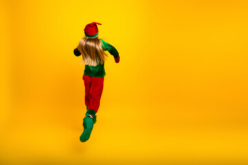 Little girl in elf costume dancing joyfully against a vibrant yellow backdrop, celebrating Christmas spirit with energy