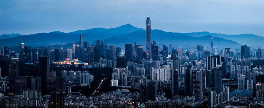 Cityscape of the modern financial district skyline with illuminated skyscrapers against a mountain backdrop at dusk in Shenzhen.