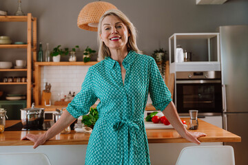 Smiling woman leaning on kitchen counter with fresh vegetables
