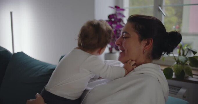 Mother kissing baby affectionately in cozy living room, natural daylight illuminating soft moment of tenderness and maternal love
