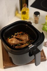 Air fryer basket with cooked chicken drumsticks, vegetables and spices on white marble countertop, closeup