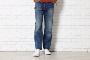 Man wearing stylish jeans near white brick wall, closeup