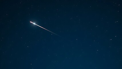 A brilliant meteor streak with a glowing tail in a star-filled night sky.  