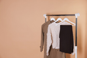 Different stylish clothes hanging on rack against beige background, space for text