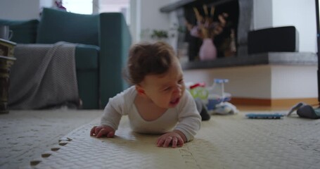 Baby lying on floor during early motor development, showing frustration while attempting to lift body and move, surrounded by toys in cozy living room
