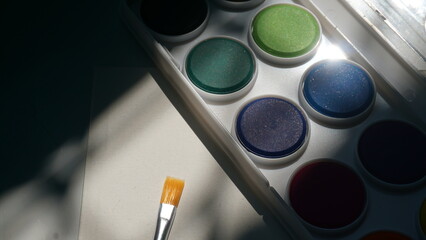 Palette of watercolor paints and a brush on a white background