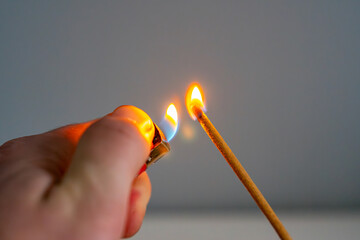 Close-up of hand lighting incense with a lighter. Bright flame adds warm accent. Detail of relaxation, aromatherapy, and calm home atmosphere.