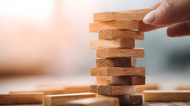 Hand carefully places wooden block atop an unstable tower structure