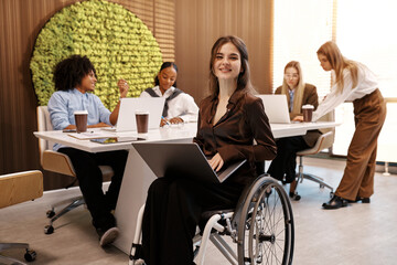 Confident woman working on laptop in modern inclusive office, using wheelchair