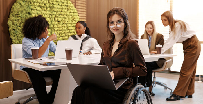 Confident woman working on laptop in modern inclusive office, using wheelchair