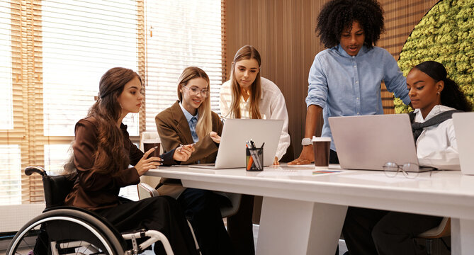Inclusive diverse business team meeting with woman using wheelchair at modern office