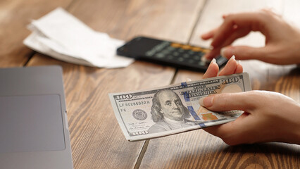 Woman holding a pile of 100 dollar bills while using calculator. Financial planning, budgeting or tax calculation concept. Ideal for personal finance, business or investment content.