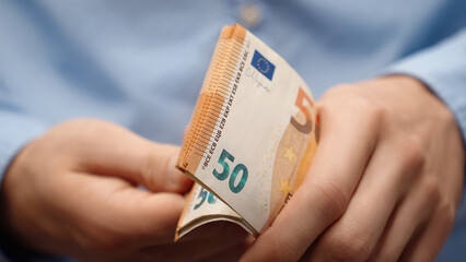 Close-up of male hands counting a pile of 50 euro banknotes. Man in blue shirt holding European...