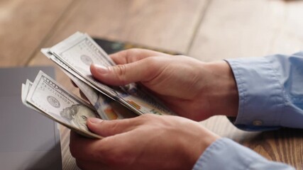 Man counting money, 100 US dollar bills while using calculator on smartphone. Financial planning, budgeting or tax calculation concept. Ideal for personal finance, business or investment content.