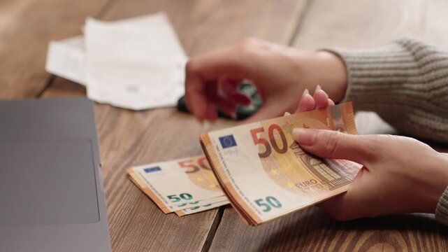 Woman counting 50 euro banknotes while using calculator. Financial planning, savings, budgeting or tax calculation concept. Ideal for personal finance, business or investment content. - Powered by Adobe